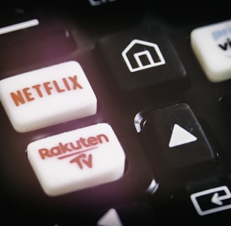A close-up of a remote control featuring buttons for various streaming services, including Netflix and Rakuten TV, along with other navigational buttons.